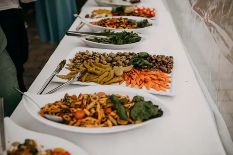 Buffet-Tisch mit verschiedenen Vorspeisen: Gemüse, Oliven, Karotten und Pasta, stilvoll angerichtet auf weißen Platten.