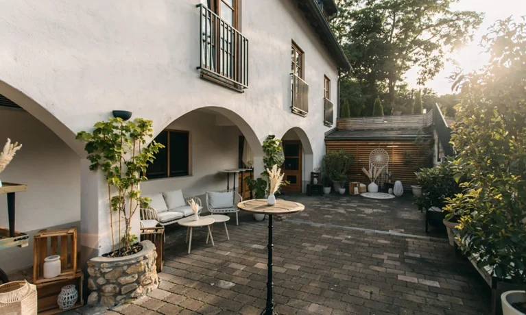 Elegante Terrasse mit Pflanzen, Sitzmöbeln und bogenförmiger Fassade bei Sonnenuntergang; idealer Ort zum Entspannen im Freien.