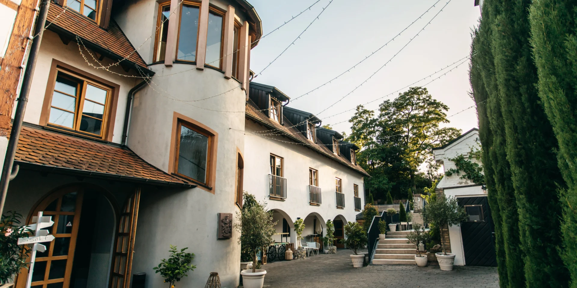 Rustikales Gebäude mit Ziegeldach und grüner Umgebung, dekoriert mit Lichterketten im Innenhof.