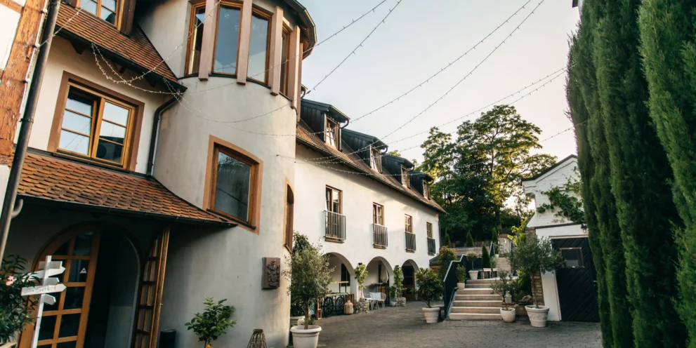 Rustikales Gebäude mit Ziegeldach und grüner Umgebung, dekoriert mit Lichterketten im Innenhof.