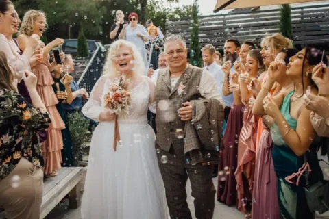 Brautpaar verlässt feierlich die Hochzeit unter einem Regen aus Seifenblasen, umgeben von applaudierenden Gästen im Freien.