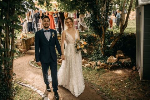 Brautpaar beim Hochzeitsauszug im Garten, umgeben von Bäumen und jubelnden Gästen.