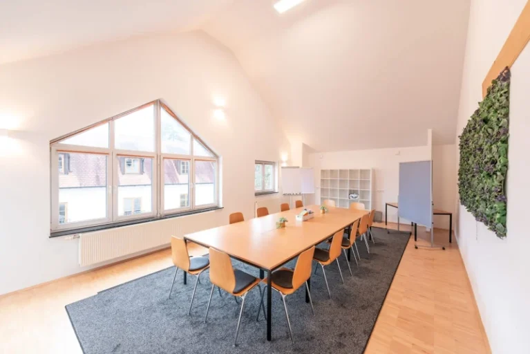 Moderner Konferenzraum mit großem Tisch, Holzstühlen, Pflanzenwand und natürlichem Licht durch große Fenster Gereon