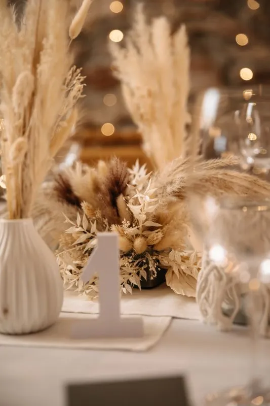Tischdekoration mit Trockenblumen und Tischkarte Nummer 1, rustikales Ambiente mit warmem Licht im Hintergrund.