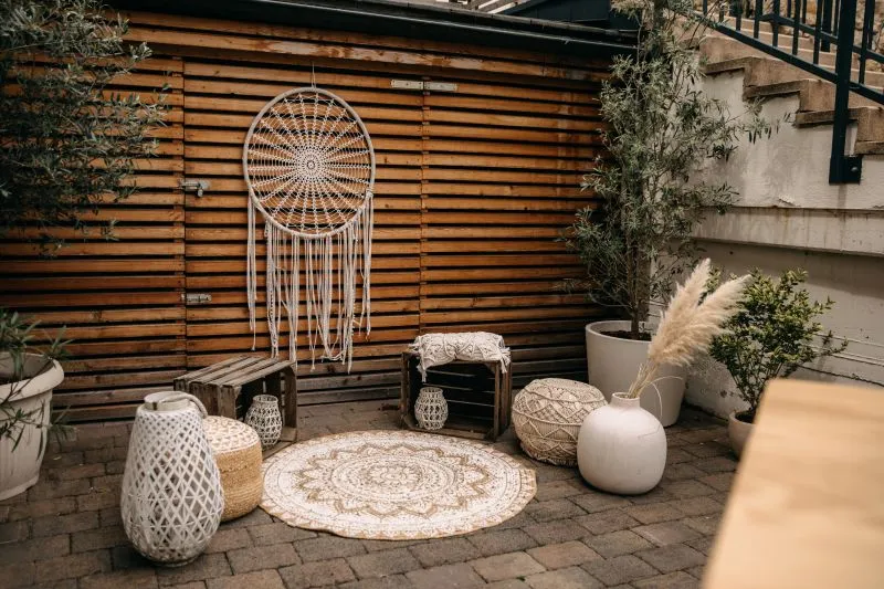 Gemütliche Terrasse mit Dreamcatcher, Sitzhockern, Laternen und Pflanzen, ideal für Boho-Style Entspannung im Freien.