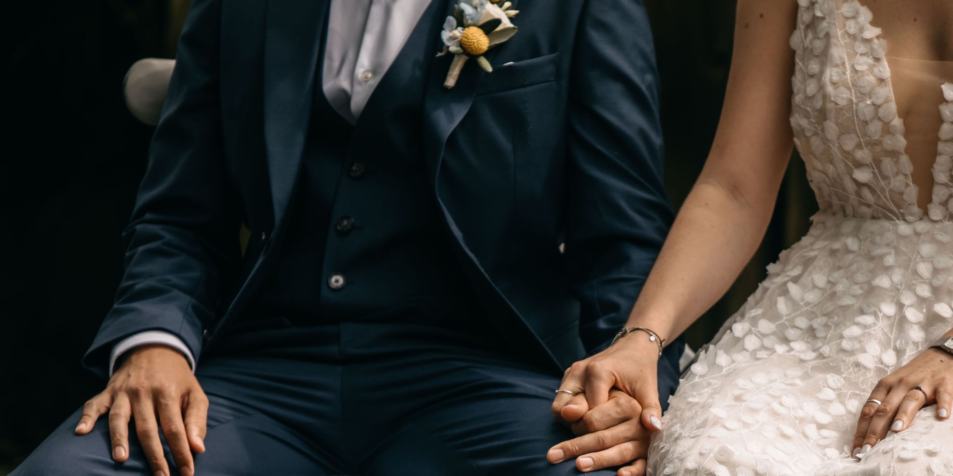 Brautpaar in eleganter Hochzeitskleidung hält Händchen, Detailaufnahme der Hände und Kleidung.